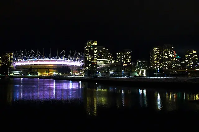 Illuminated stadium and city skyline reflected in the water at night